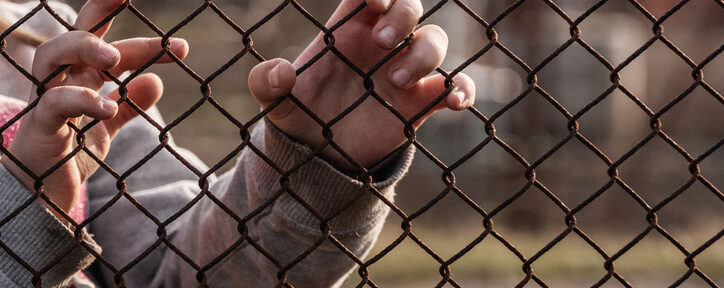 child's hands at chainlink fence