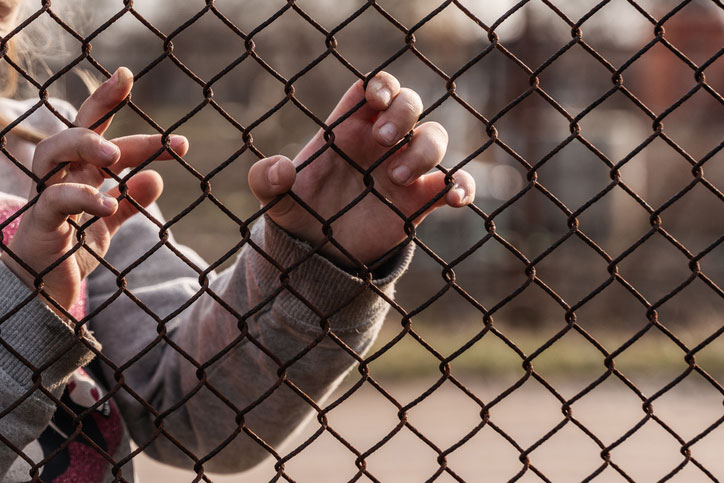 child's hands at chainlink fence